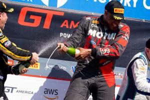 Racecar driver Robb Holland spraying a bottle of champagne in celebration.