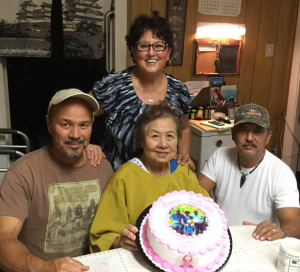 Older woman holding birthday cake surrounded by her 3 adult children