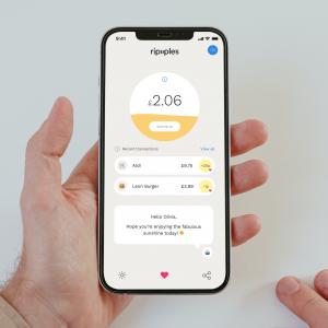 A photograph of someone holding a phone that displays Ripples app. The Ripples app is showing penny donations from roundups