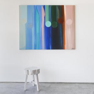 Abstract painting with hues of blue, pink, green, and brown. The painting is hung above a white wooden stool