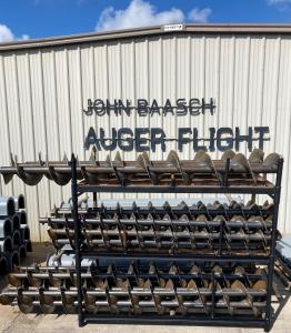 a rack of auger flighting in front of a building with aluminum siding that says John Baasch Auger Flight