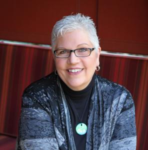 Grey haired woman wearing a mom necklace is smiling,