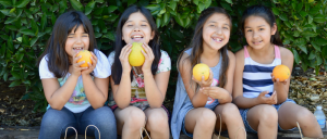 group of young girls smiling sitting holding oranges