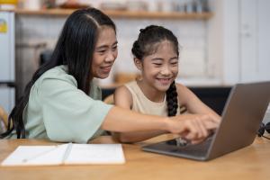Asian woman tutoring a girl on a laptop computer.