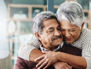 A woman stands behind a man and wraps her arms around him. People who need disability benefits can get help from professional representatives.