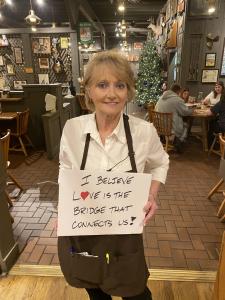 Woman holds up a sign that says,"We don’t have to always agree with one another to love one another.”