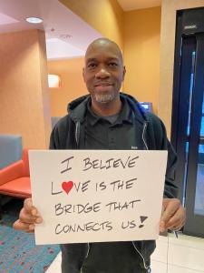A man holds up a sign that says love is the bridge that connects us.