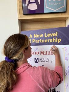 Student symbolically signing $130 million dollar agreement between Avila University and KC Scholars