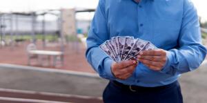Man wearing dress pants and buttoned shirt counts money while standing in a workout area.
