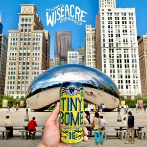 A photo of a can of Tiny Bomb pilsner being held in front of the iconic "Bean" sculpture in Chicago's Millennium Park.