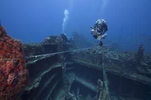 A person in dive gear using equipment to document wreckage underwater.