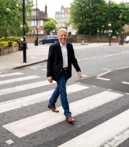 Ed in black suit walks across the famous zebra striped crosswalk