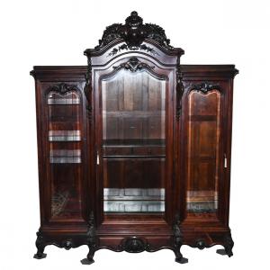 Massive, three-door rosewood china cabinet, 112 inches tall by 93 inches wide, having an elaborate crest with a monogram “B”, beveled glass doors and glass shelves. The cabinet is of the highest quality.