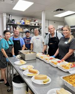 Six people are in the commercial kitchen at Cape Vineyard community church preparing hot meals for the community.