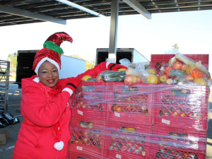 Fausat Rahman-Davies wears a Christmas outfit and stands beside a pallet of produce.