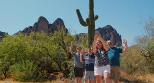 A family standing in front of a catus. They all have hands up smiling, excited and cheering.