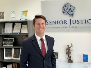 Attorney Garrick Harding standing in front of the Senior Justice Law Firm logo