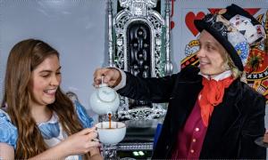 Mad Hatter in top hat pouring Alice a cup of tea from a blue teapot