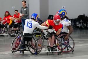 Two Los Angeles Rams Wheelchair Football Team players surround a player with the Kansas City Chiefs Wheelchair Football Team with the ball