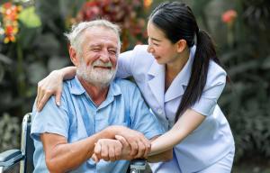 Elderly man in a wheelchair smiles at a home health aide.