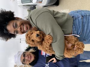 A pet owner smiles at the camera while holding her fluffy brown dog. An event volunteer smiles alongside her.