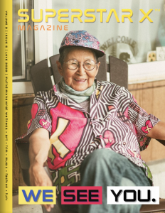 Two-Spirit Ojibwa-Cree Elder, Ma-Nee Chacaby, is on the cover of Superstar X Magazine; a digital publication. Smiling, Elder Ma-Nee is wearing glasses, a colourful top and hat, with jeans. There is "We See You" text on the cover of the magazine.
