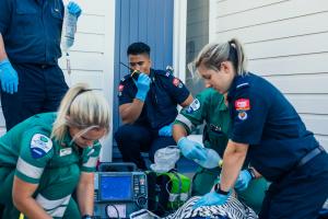 The photo shows New Zealand ambulance and fire service staff at a simulated exercise reviving someone who is playing the part of an accident victim. Two officers are holding Tait Communications portable radio units.