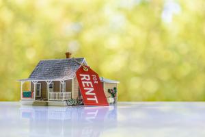 Model house with a paper tag reading 'for rent' attached with a chain