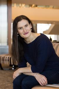 Jodi Daniels, founder of Red Clover Advisors sitting on a light colored couch, leaning forward and wearing a dark colored shirt adn jeans.