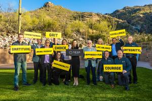 The Sun Company team members hold up bright yellow signs that state the company's 11 core values in bold black letters - connectedness, grit, integrity, life balance, excellence, gratitude, courage, happiness and fun, responsibility, choice, and being pre