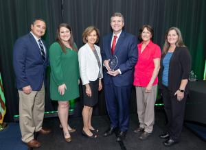 Tuscaloosa Mayor Walt Maddox standing onstage receiving a new national disaster leadership award along with LeadersLink Founder Kathleen Koch and family members of late Waveland, Mississippi Mayor Tommy Longo who the award is named after.