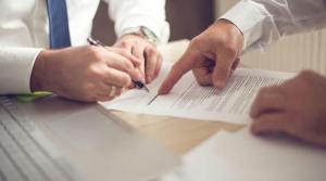 The hands of two men in business shirts point to and write on documents on a desk, with a laptop on one side. Disability lawyers help people sort through the complexities of long-term disability insurance claims and Social Security Disability benefits.