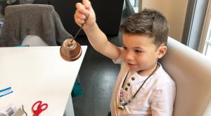 Boy holds a handmade bell while wearing a bell necklace.