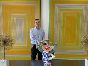 Man in a button up shirt standing in amid large, colorful paintings and sculptures at Palm Beach Modern Auctions