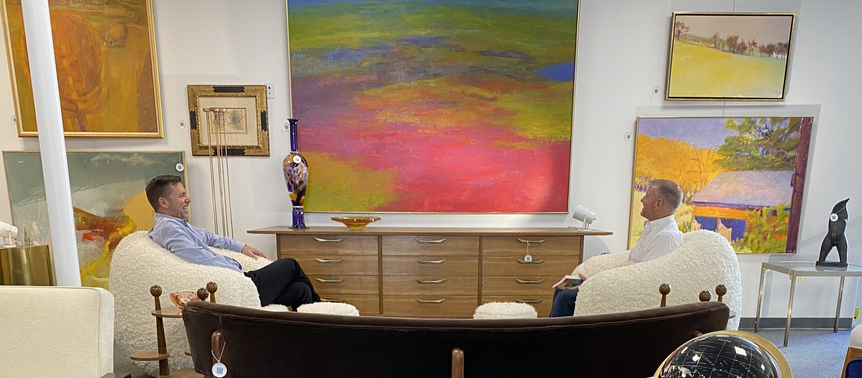 Two men seated on a large sofa in front of colorful abstract art at Palm Beach Modern Auctions