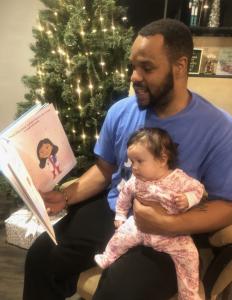 Father reading The Sandbox Series to his daughter while she sits on his lap.