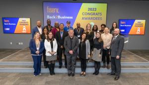 18 people of varied backgrounds stand on or near podium looking into the camera