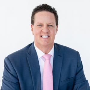 James Malinchak Headshot wearing a dark blue suit, white shirt and pink tie