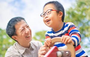 A father plays at a playground with his son, both smiling. Families can get help from special needs planning lawyers to create special needs trusts that protect access to government benefits.