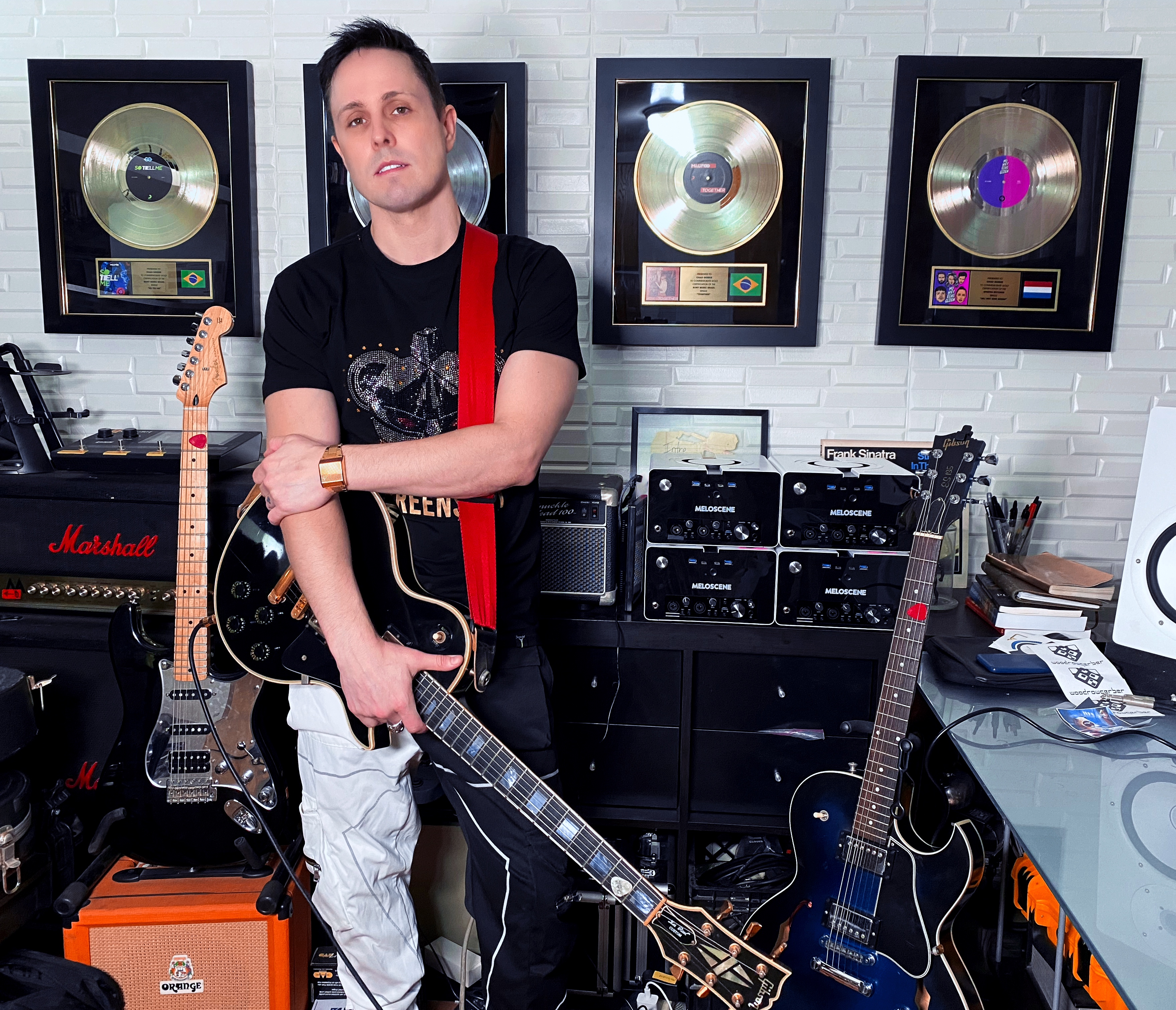 Musician Chad Gerber standing with his guitar in his personal studio in front of his gold and platinum records and a stack of his VR interface SceneKeys