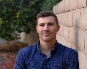 Brandon Lucero, founder of New Generation Mastery Podcast poses next to wall