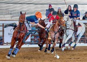 an arena polo player reaches out for the ball while a defender attempts to stop him with his mallet.  Both are on horses