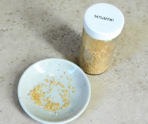 Sesame seeds in a small bowl next to a spice bottle labeled "Sesame"