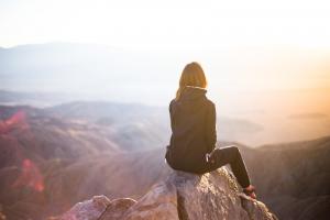 A woman sitting on top of gray rock overlooking mountain contemplating what she learned with Dr. Sydney Ceruto in her Brain-Based Coaching session.