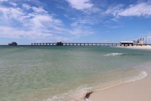 Sandy beach and green/blue waters with pier in the distance