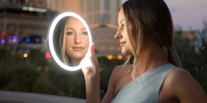 model handholding mirror that detaches from countertop or wall base standing on the Las Vegas strip and we see gorgeous bright light on her face and her reflection in the mirror