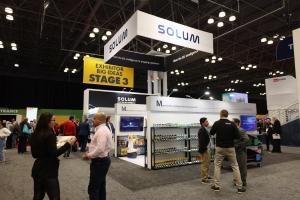 A photo of SOLUM Booth at NRF 2023, with the SOLUM signage hanging over LED screens and product displays.