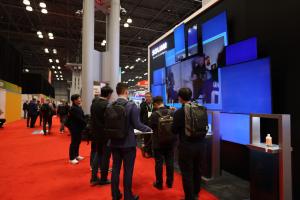 A group of visitors looking at the displays of LED TVs mounted on the SOLUM Booth wall.