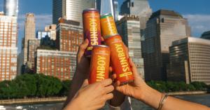 Four hands cheersing cans of SUNBOY Spiked Coconut Water in front of the New York City skyline