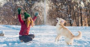 Woman in snow clothes is playing with her dog in the snow